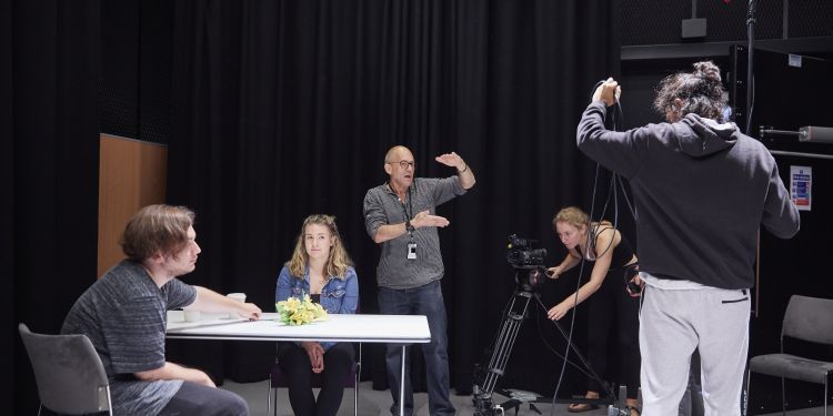 男女演员坐在表前准备拍场景主管站在他们身后,用他的臂教摄像师和Homa操作员如何搭建镜头